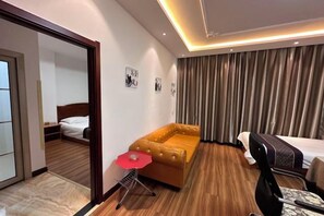 A hotel room with a wooden floor, a brown sofa, a bed, a desk with a chair, and a red umbrella.