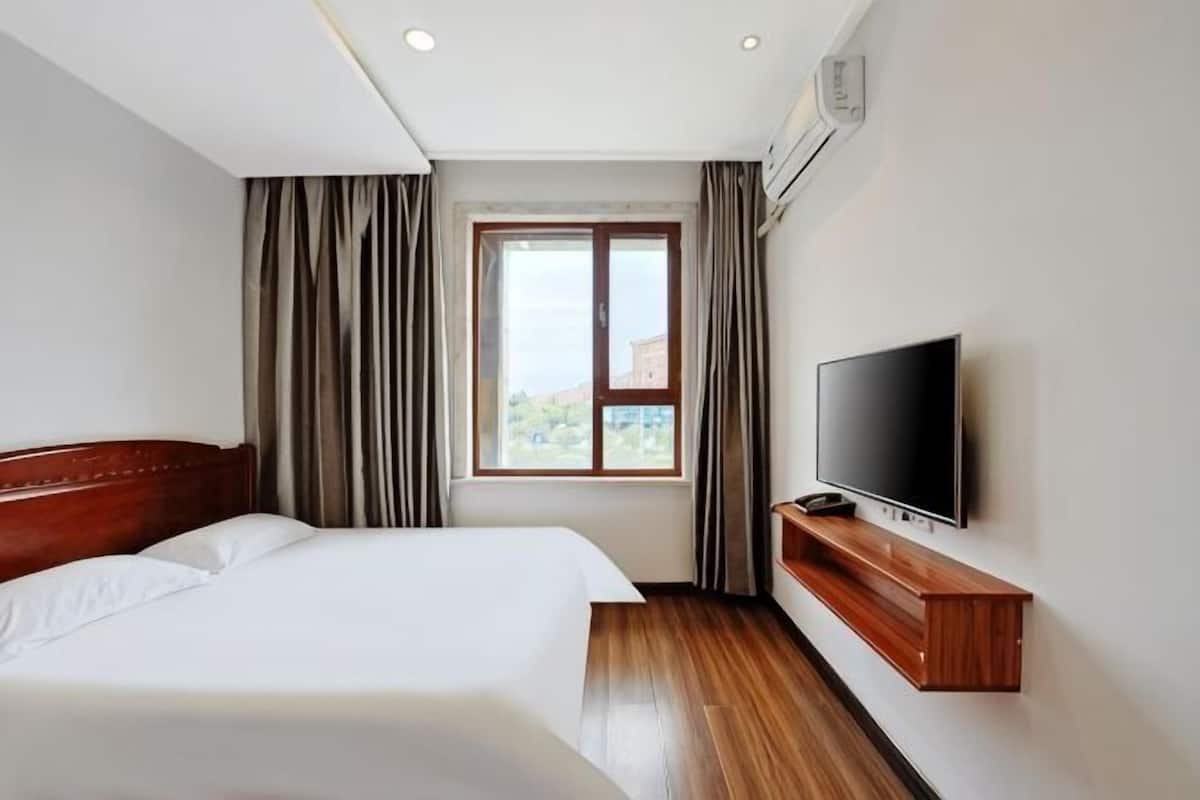 Habitación de hotel con cama, televisor, ventana con cortinas y vistas al exterior.