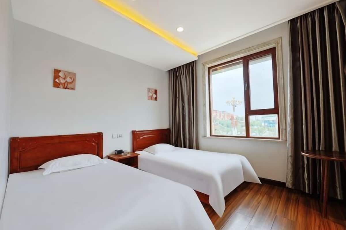 Habitación de hotel con dos camas, una ventana con cortinas y vistas al exterior.