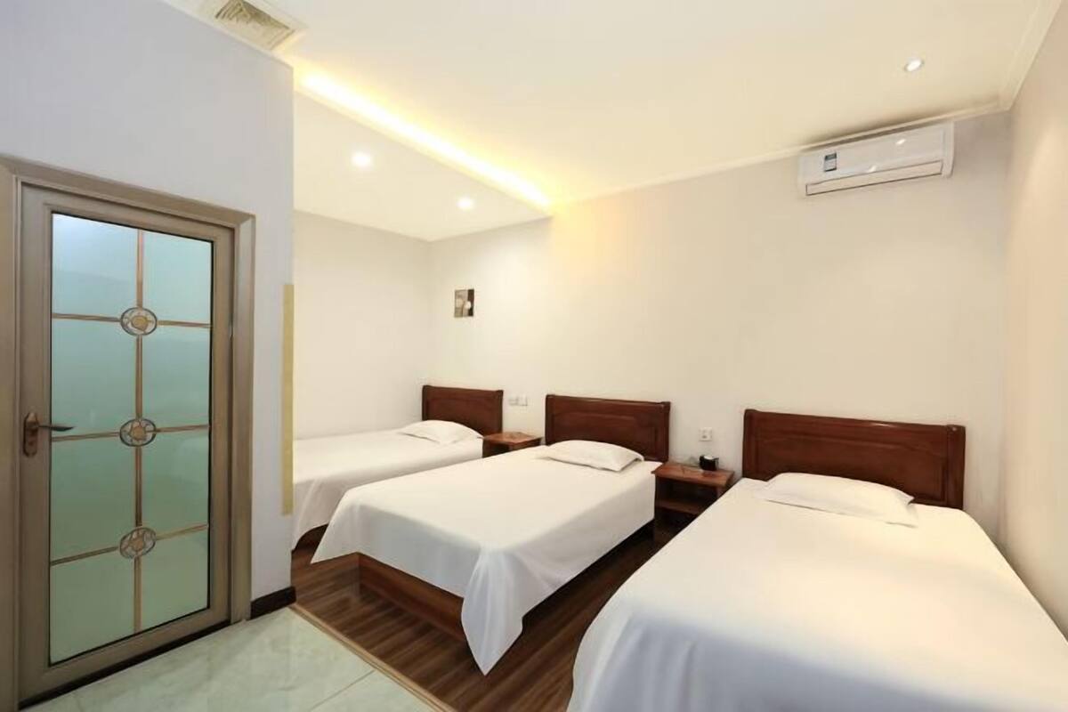 Una habitación de hotel con dos camas individuales, piso de madera, una puerta con paneles de vidrio esmerilado y un equipo de aire acondicionado en la pared.