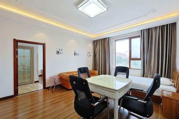 Une chambre d’hôtel comprenant une table à manger, des chaises, un canapé, un lit, une fenêtre avec des rideaux et une porte donnant sur une autre pièce.