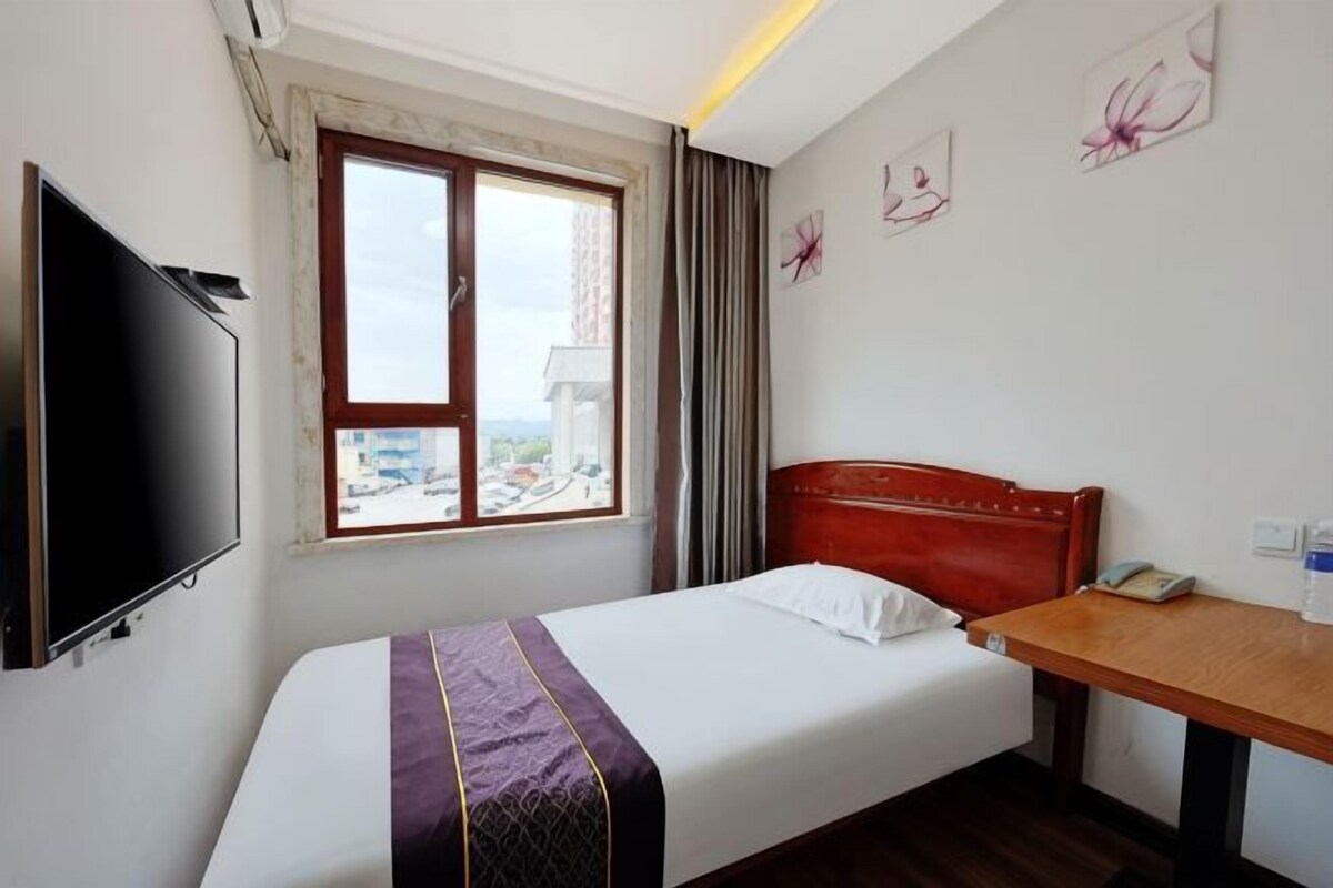 A hotel room with a bed, a TV, a window, and a desk.