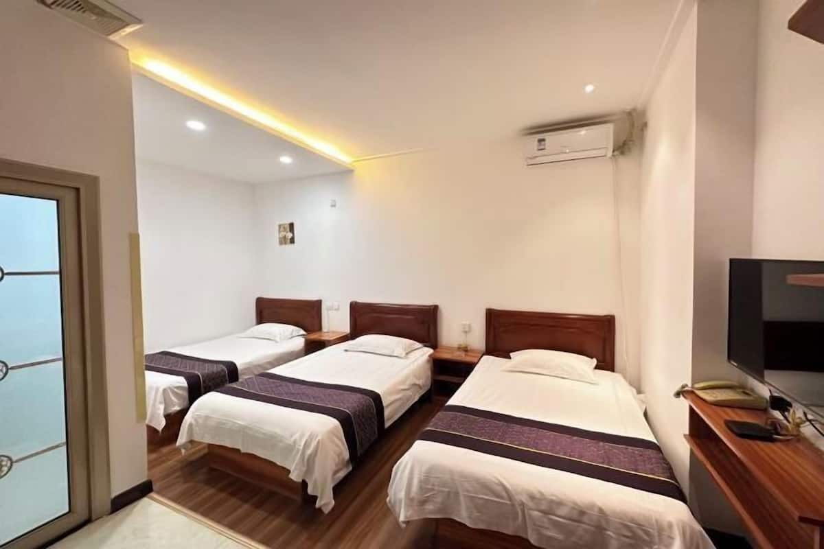 Habitación de hotel con tres camas individuales, suelo de madera, un televisor sobre una mesa de madera y un equipo de aire acondicionado en la pared.