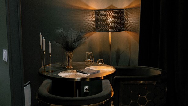 A round bar area with a black and gold design, a hexagonal patterned chair, a round table with a black surface, a feathered vase, and a textured lamp. - Romantic Night Getaway (Cherbourg-en-Cotentin)