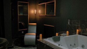 A modern bathroom with a marble floor, a black leather chair, a large bathtub, and two wall-mounted mirrors. - Romantic Night Getaway (Cherbourg-en-Cotentin)
