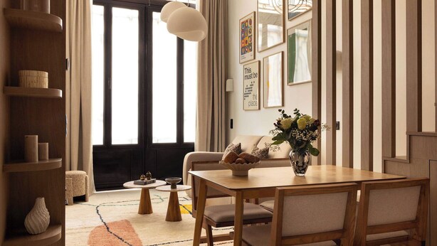 Un comedor acogedor con una mesa y sillas de madera, un florero con flores y una alfombra.