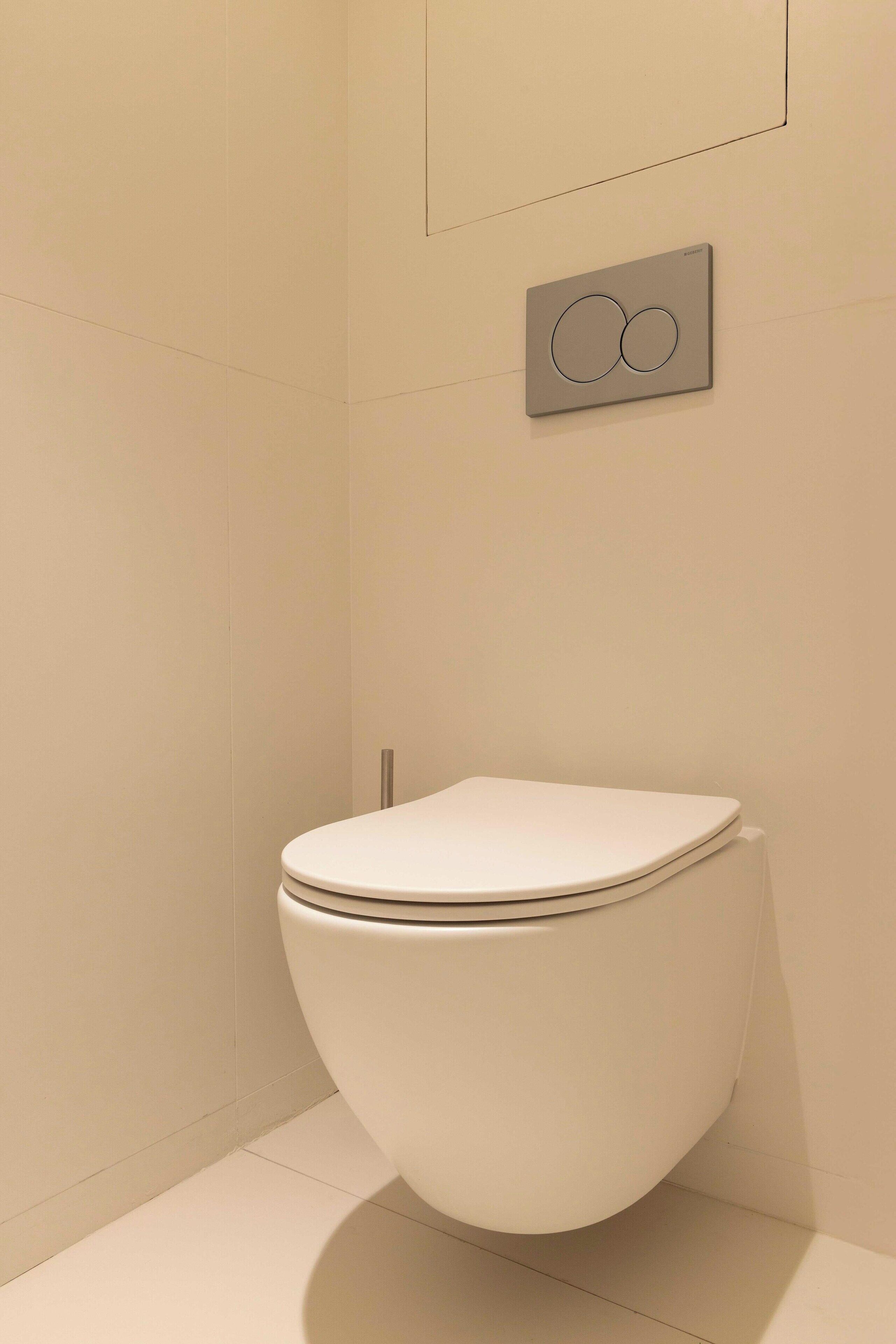 Un inodoro moderno con un diseño elegante, un accionador de descarga empotrado en la pared y un baño limpio y minimalista.