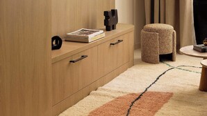 Una sala de estar moderna con un televisor de pantalla plana montado en una pared de madera, un pequeño reposapiés y una estantería con libros y un objeto decorativo.