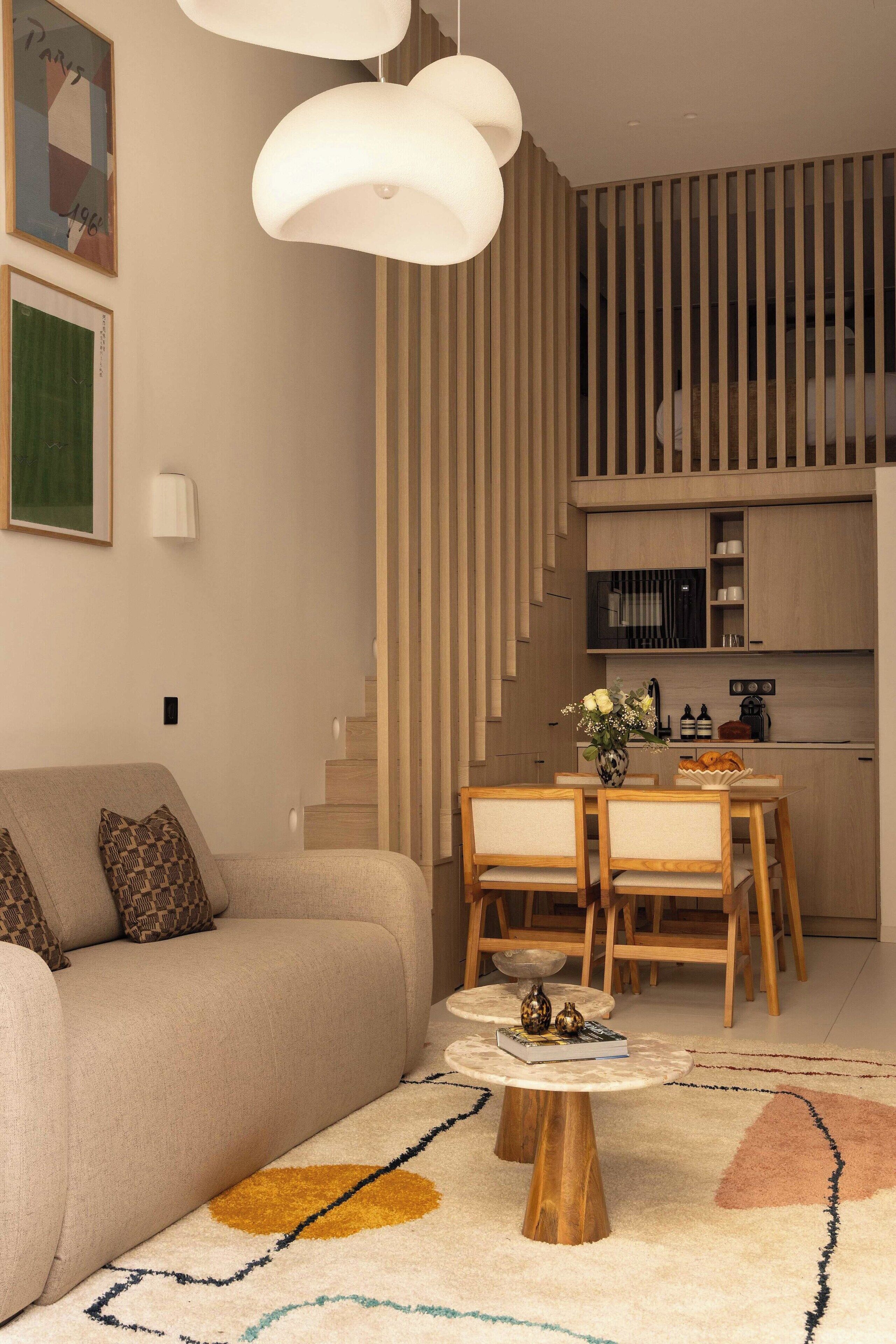 A modern living room with a sofa, a dining table with chairs, a coffee table, and a kitchen area with wooden cabinets and a microwave.