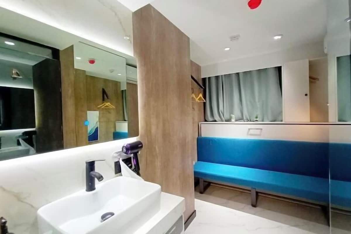 A modern bathroom with a large mirror, a white sink, and a blue bench.