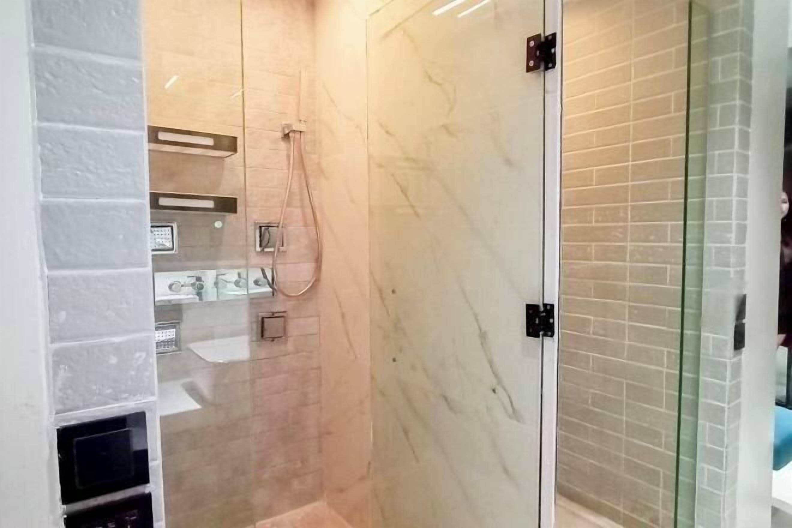A modern bathroom with a glass shower enclosure, marble walls, and built-in shelves.