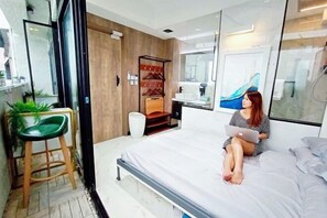 A modern bedroom with a bed, a laptop, a green chair, a wooden cabinet, and a glass shower area. - Harbour Hella Inn (Hong Kong)