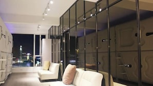 A modern hotel room with a city view, a sofa, a chair, and a glass partition.
