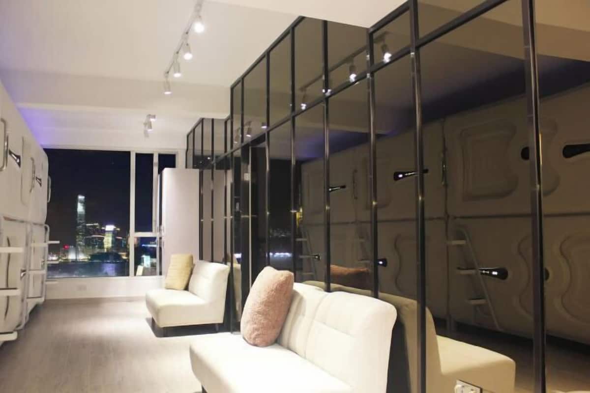 A modern hotel room with a city view, a sofa, a chair, and a glass partition.