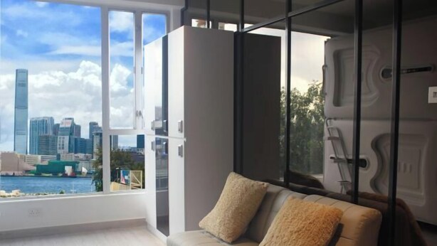 A modern living room with a sofa, a glass partition, and a view of a city skyline.