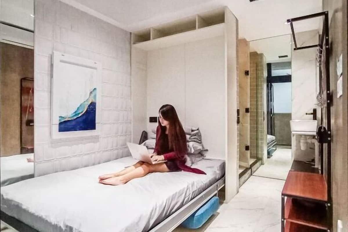 A modern bedroom with a bed, a desk, and a bathroom in the background.