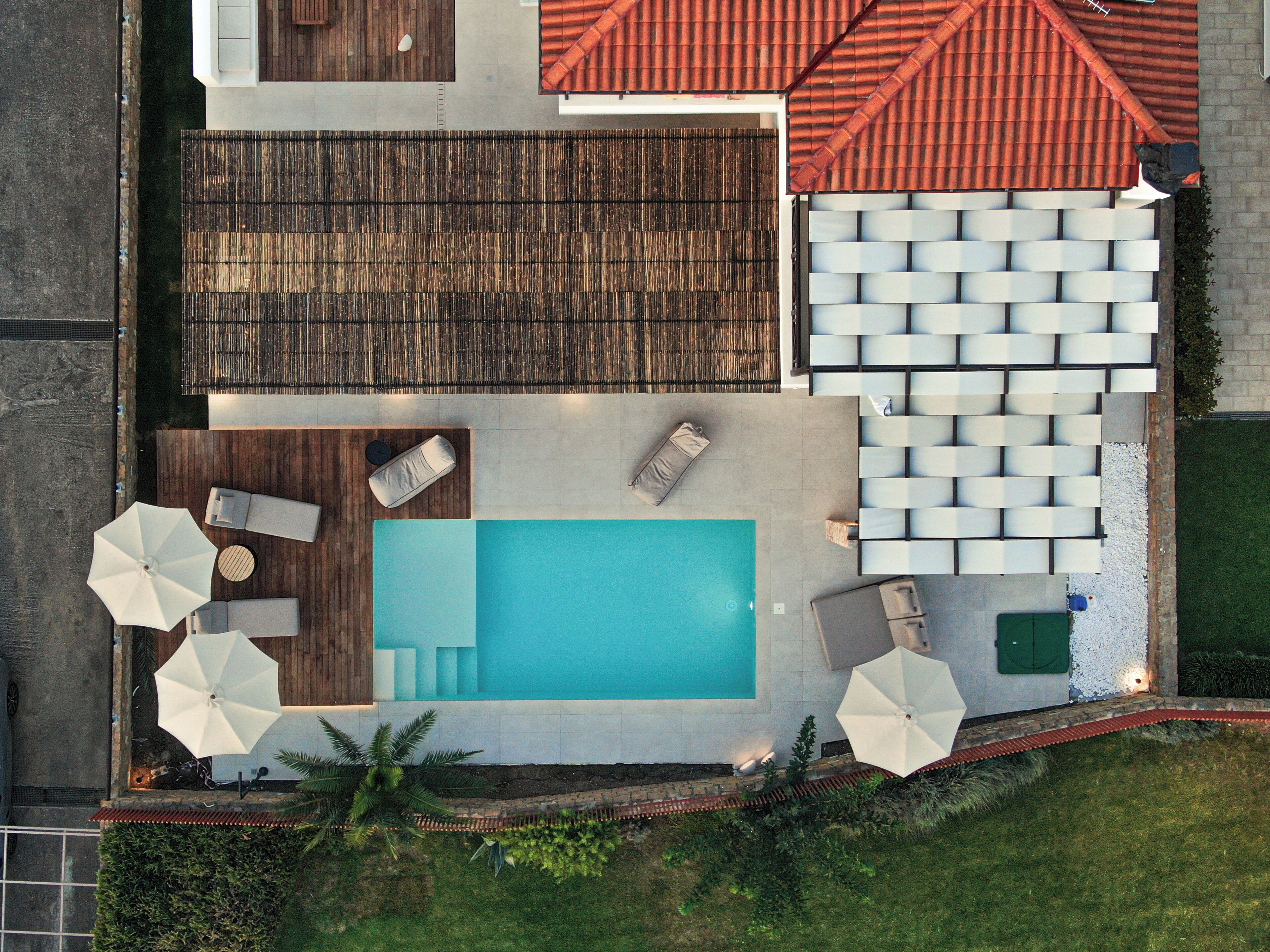 Ein Poolbereich auf dem Dach mit einem rechteckigen Pool, Liegestühlen, Sonnenschirmen und einer Sitzecke mit weißen Tischen und Stühlen.