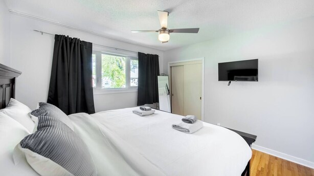 A hotel room with a large bed, a ceiling fan, a flat-screen TV, and a window with curtains. - Beautiful Home In A Prime Location (Winnipeg)