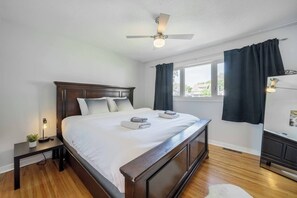 A neatly made bed with white linens and two towels, a wooden headboard, a bedside table with a lamp, and a ceiling fan. - Beautiful Home In A Prime Location (Winnipeg)