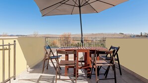A patio with a table and chairs, an umbrella, and a view of trees and buildings. - La TOSCANELLA - Terricciola house -House with garden (Selvatelle)