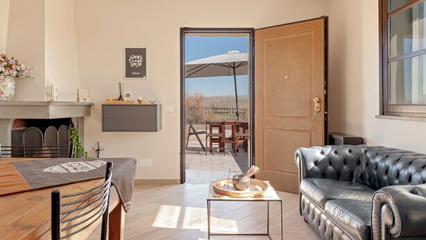 A modern living room with a fireplace, a dining area with a wooden table and chairs, a leather sofa, and a view of the outdoors through an open door. - La TOSCANELLA - Terricciola house -House with garden (Selvatelle)
