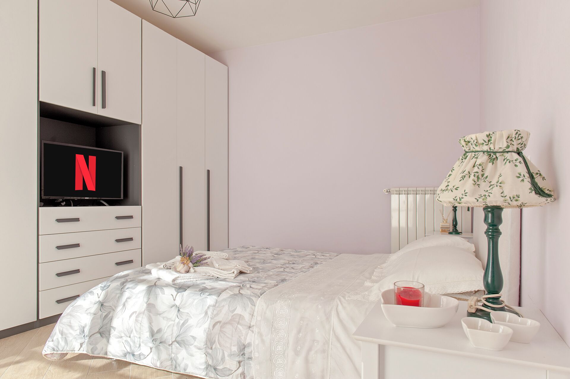Camera da letto con un letto, una TV, una lampada e un comodino con un bicchiere di liquido rosso.