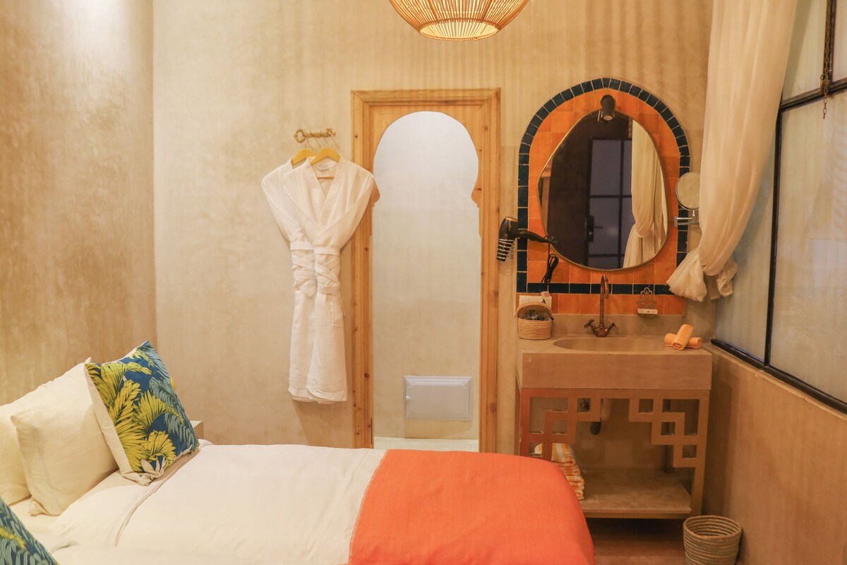 A hotel room with a bed, a bathroom with a mirror, and a towel rack.