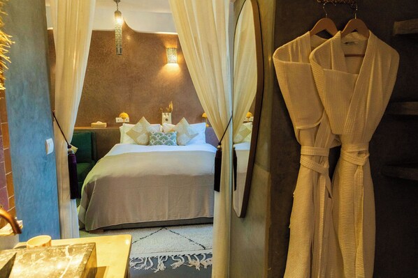 A hotel room with a bed, a robe hanging on the wall, and a mirror. - Riad 10 Mandarin (Marrakech)