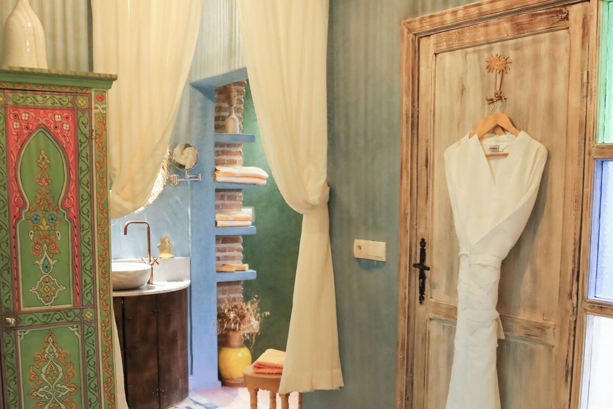 A room with a patterned floor, a wooden door, a hanging robe, and a cabinet with decorative elements.