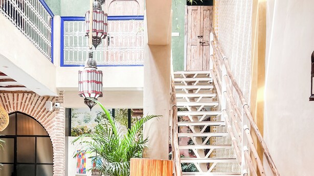Un espace intérieur spacieux avec un escalier en bois, une grande plante en pot et une lanterne suspendue.