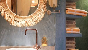 Une salle de bain avec un miroir rond, un robinet en cuivre, un lavabo en forme de coupe et une pile de serviettes sur une étagère.