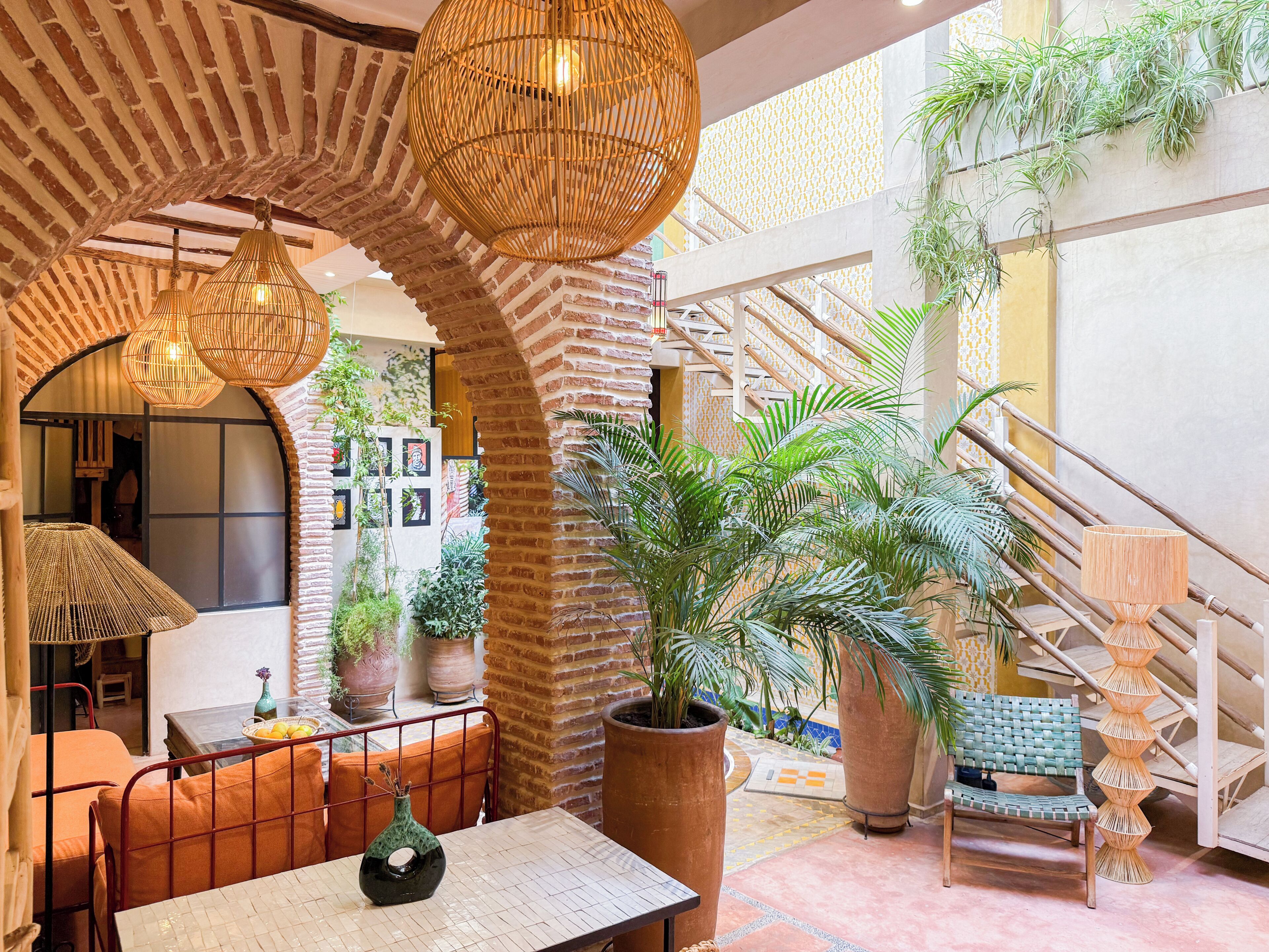 Un espacio interior amplio con pared de ladrillo, una escalera y diversas plantas en macetas.