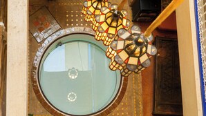 Une lucarne circulaire ornée de motifs en mosaïque, un lustre suspendu et un sol à motifs.