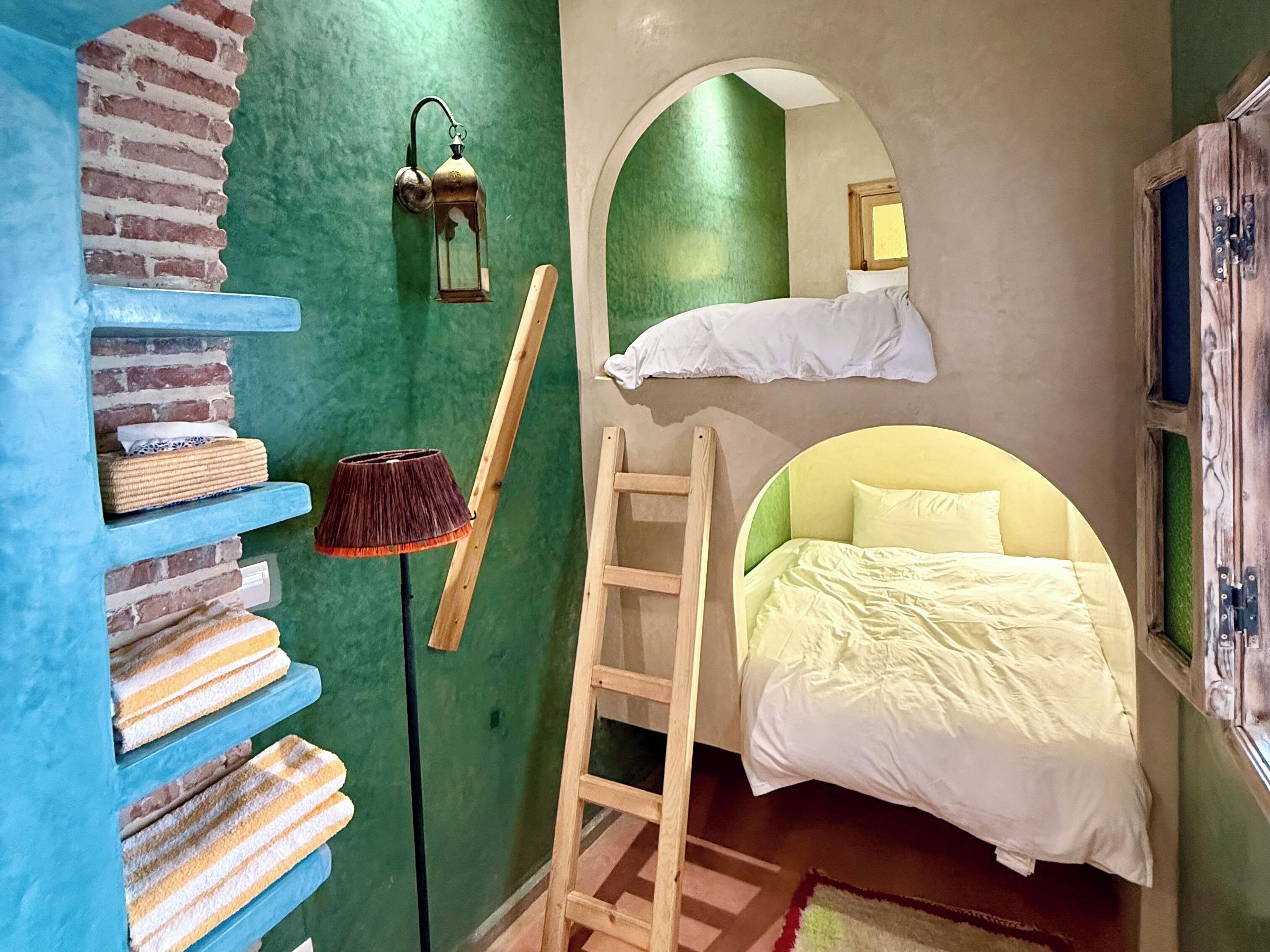 Une chambre avec un lit superposé, une échelle, une étagère avec des serviettes, une lampe et une lanterne fixée au mur.