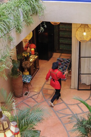 Um saguão de hotel com piso ladrilhado, balcão de recepção e uma pessoa caminhando.