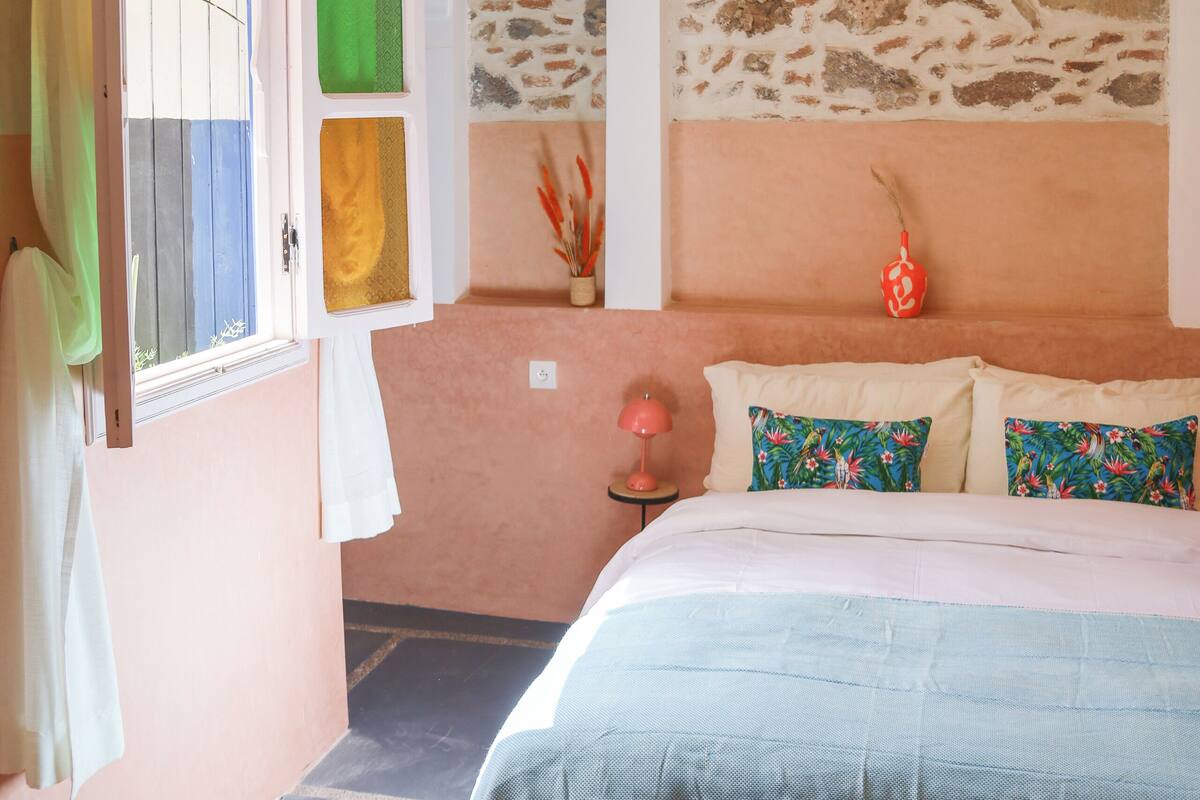A bedroom with a bed, a geometric pendant light, a window with curtains, and a stone wall.