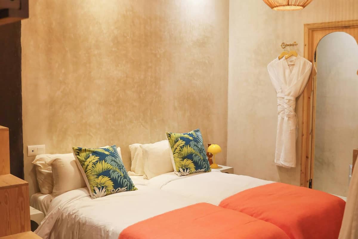 A bedroom with a bed, two bedside tables, a wooden chair, a mirror, and a hanging robe.