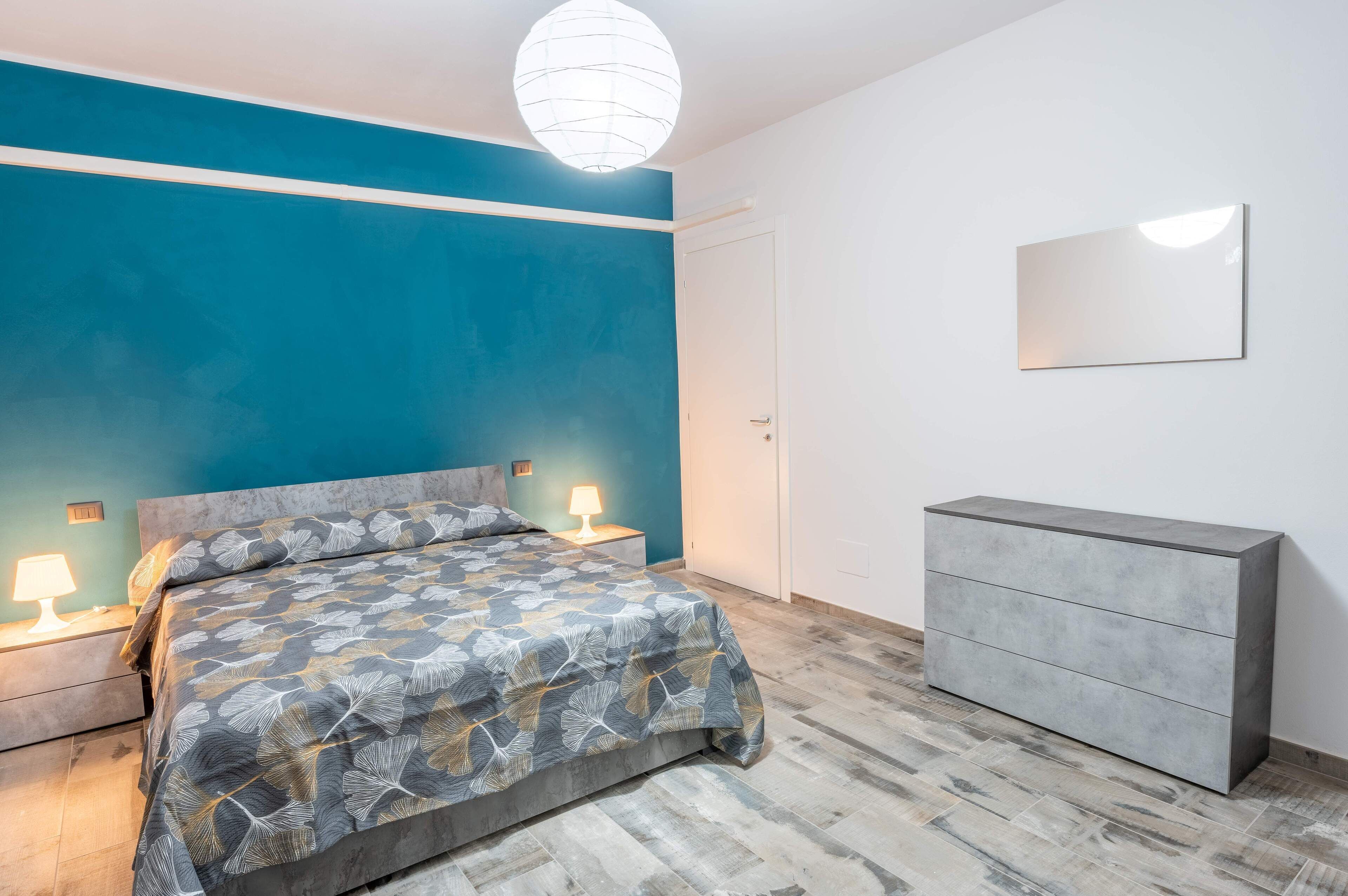 A bedroom with a bed, bedside lamps, a dresser, and a wall-mounted mirror.