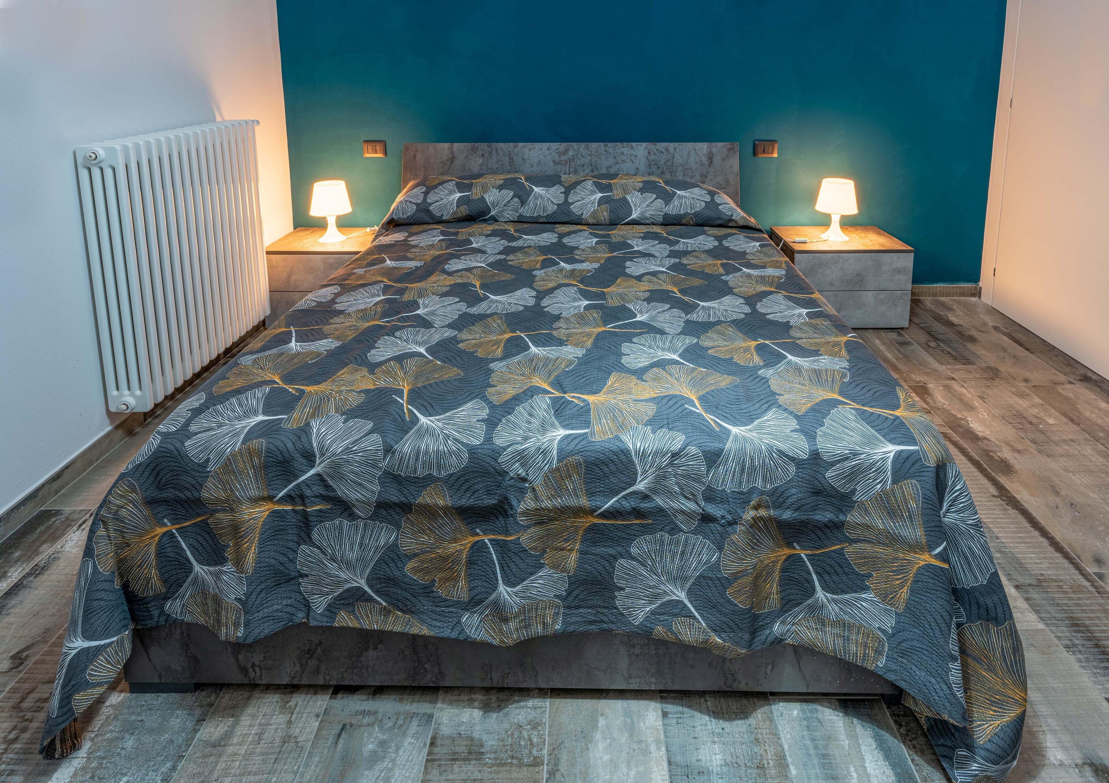A bedroom with a bed, two bedside lamps, a radiator, and a nightstand.
