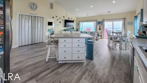 A spacious kitchen with a central island, white cabinetry, and a large window offering a view of the ocean.
