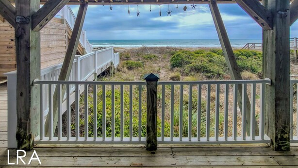 A wooden deck with a view of the beach and ocean.