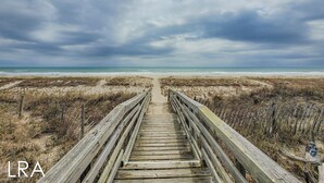A wooden boardwalk leading to a beach with overcast skies.