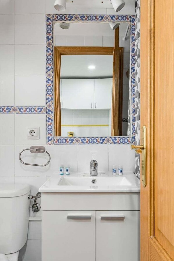 Une salle de bain avec un lavabo blanc, un miroir doté d’un cadre décoratif, des toilettes et une porte en bois.