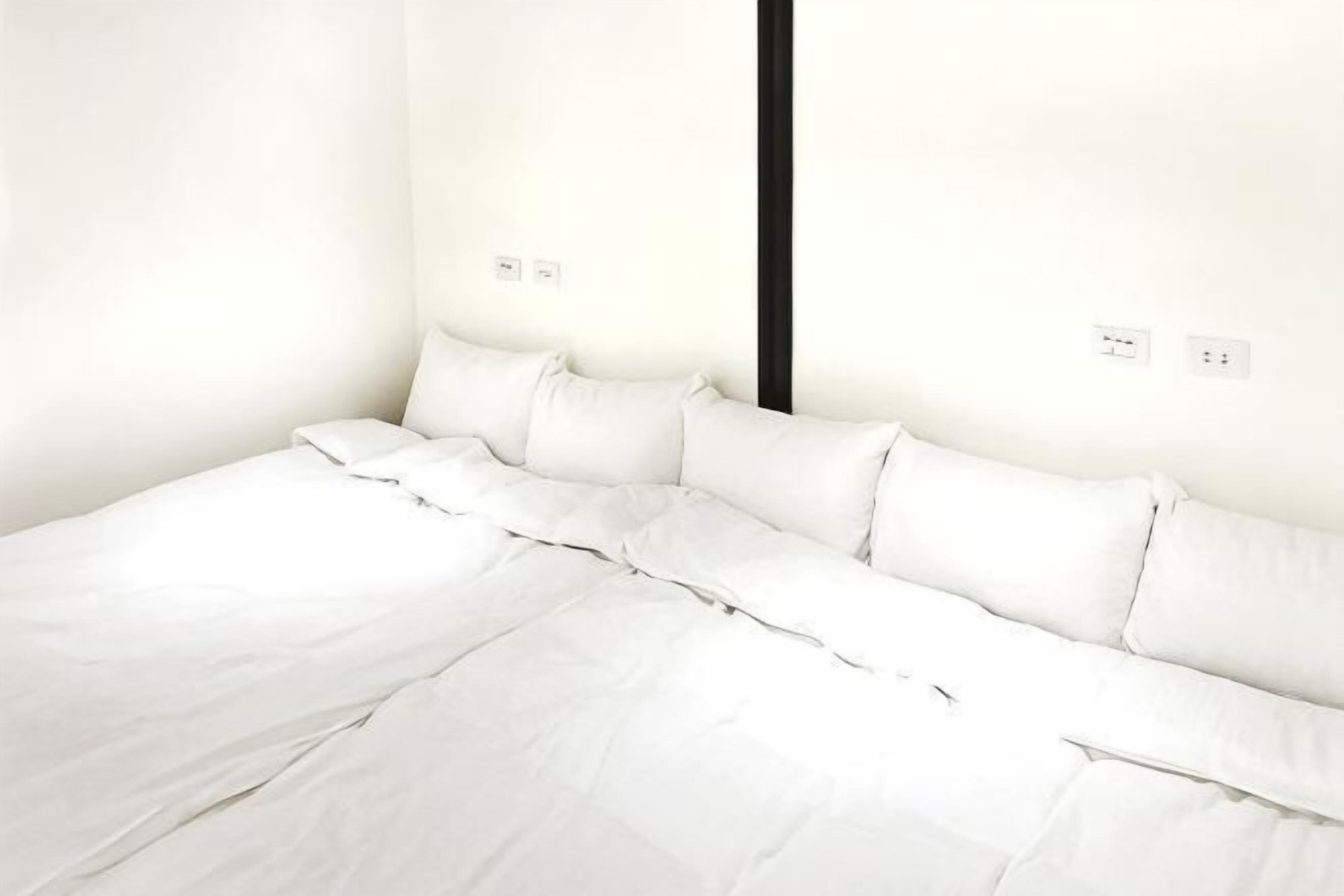 A bed with white bedding in a room with white walls and a black vertical element.