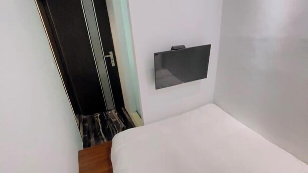 A small, simple room with a bed, a wall-mounted TV, and a door leading to another room. - Ching Shang Tien Hua (New Taipei City)