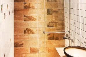 Et badeværelse med en flisebeklædt væg med forskellige arkitektoniske motiver, en vask og en håndklæderadiator.