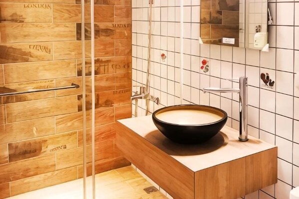 A bathroom with a wooden vanity, a black bowl sink, and a glass shower enclosure.