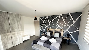 A modern bedroom with a geometric-patterned wall, a bed with a wooden headboard, a bedside table, and a hanging light fixture.