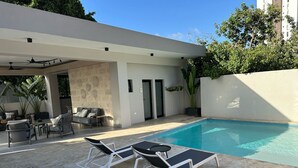 A modern outdoor pool area with lounge chairs, a seating area with sofas, and a stone wall. - Beautiful  luxury apartment  (Santiago de los Caballeros)