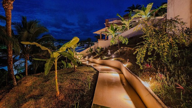 A nighttime view of a hillside with a water slide, palm trees, and a building with a red roof.